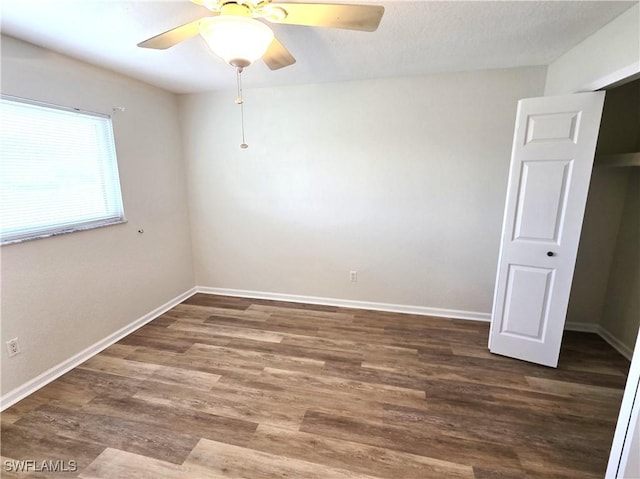 unfurnished room with a ceiling fan, baseboards, and dark wood-type flooring