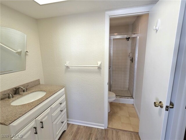 full bath featuring toilet, a shower stall, vanity, wood finished floors, and baseboards