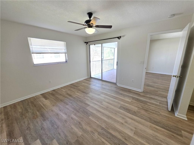 empty room with ceiling fan, a textured ceiling, baseboards, and wood finished floors