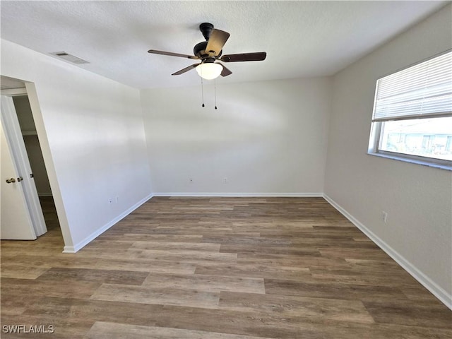 empty room with baseboards, visible vents, ceiling fan, wood finished floors, and a textured ceiling