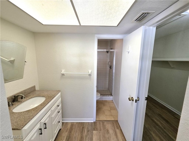 full bath with visible vents, toilet, vanity, a shower stall, and wood finished floors