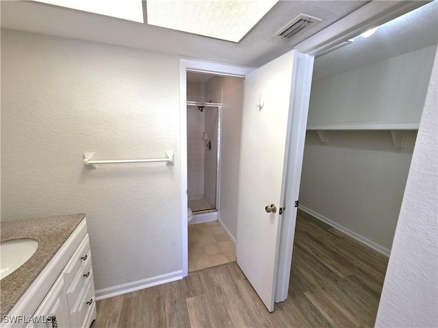 full bath featuring visible vents, a stall shower, vanity, wood finished floors, and baseboards