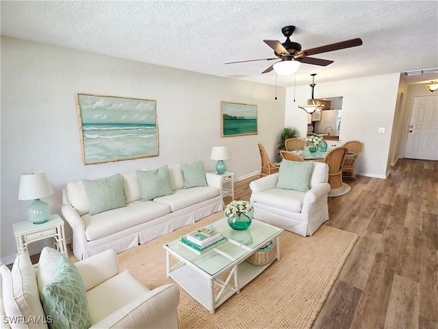 living area with ceiling fan, a textured ceiling, baseboards, and wood finished floors