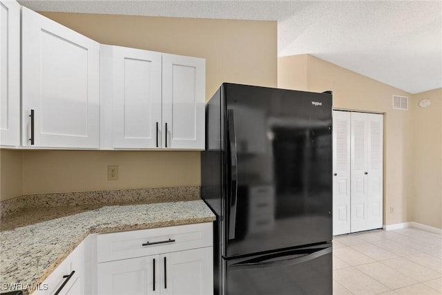 kitchen featuring visible vents, white cabinetry, freestanding refrigerator, light tile patterned floors, and light stone countertops