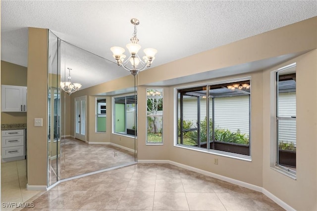 interior space with baseboards, a notable chandelier, light tile patterned flooring, and a textured ceiling