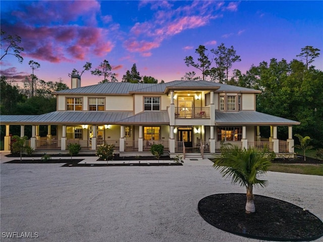 rear view of property featuring a standing seam roof, metal roof, a balcony, covered porch, and a chimney