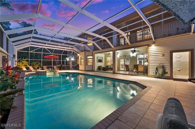 pool at dusk with a lanai, a patio area, a pool with connected hot tub, and a ceiling fan