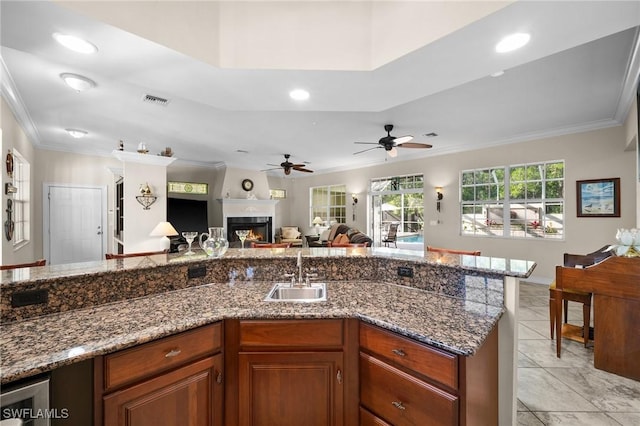 kitchen featuring a sink, visible vents, open floor plan, a lit fireplace, and crown molding