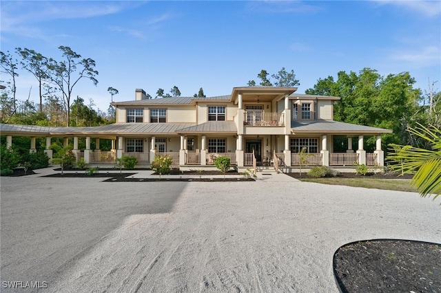 view of front of house featuring a chimney, a standing seam roof, metal roof, and a balcony