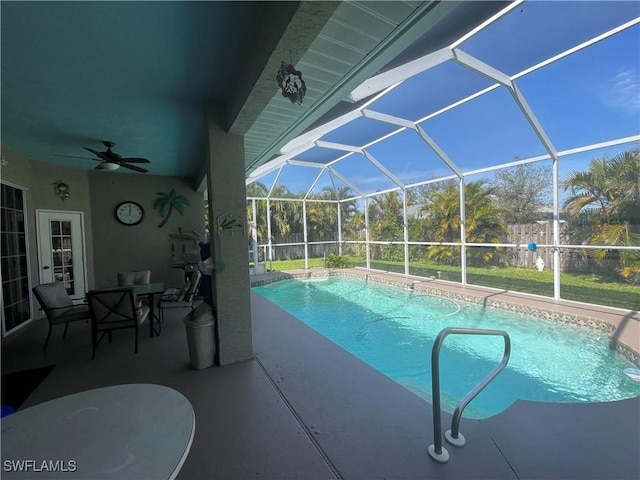 outdoor pool with glass enclosure, a patio area, and a ceiling fan