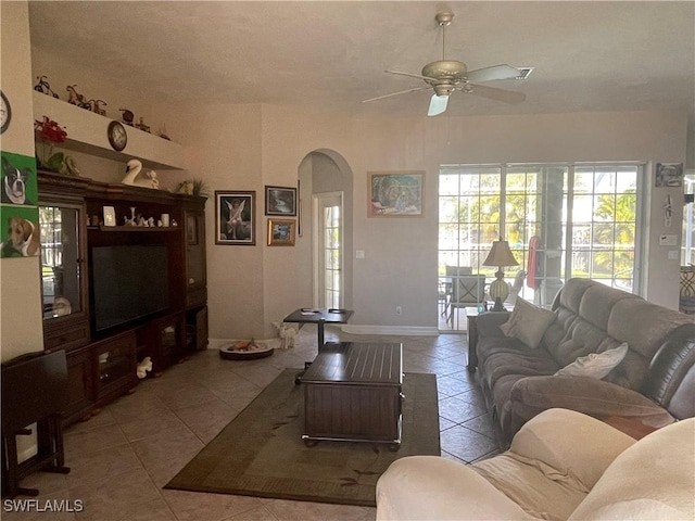 living room featuring a ceiling fan, arched walkways, light tile patterned flooring, and baseboards