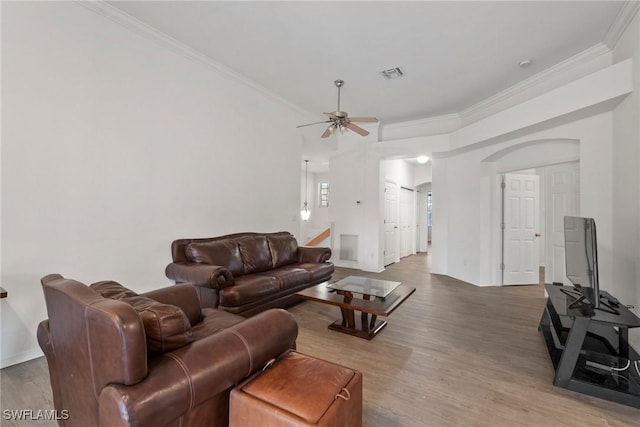 living area featuring visible vents, arched walkways, a ceiling fan, wood finished floors, and crown molding
