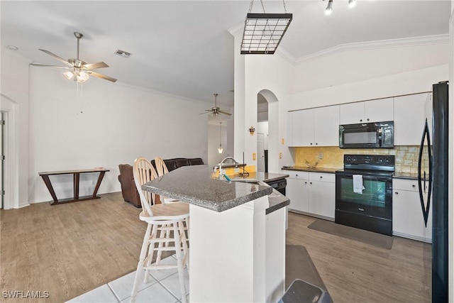 kitchen featuring visible vents, white cabinets, arched walkways, dark countertops, and black appliances