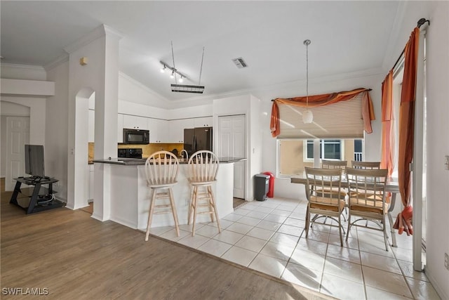 kitchen featuring visible vents, white cabinets, black appliances, dark countertops, and crown molding