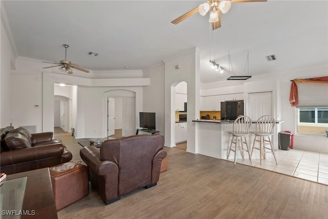living area with light wood finished floors, visible vents, arched walkways, and crown molding