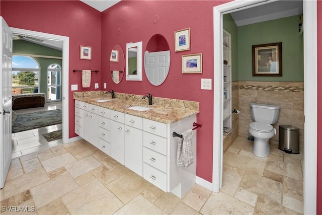 bathroom with double vanity, a sink, toilet, and stone tile floors