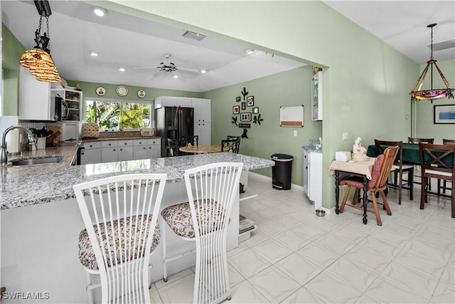 kitchen with a peninsula, a sink, white cabinets, black fridge, and pendant lighting