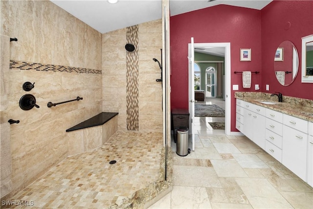 bathroom with baseboards, stone finish floor, vaulted ceiling, vanity, and a walk in shower