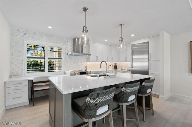 kitchen with wall chimney exhaust hood, appliances with stainless steel finishes, a sink, and white cabinetry