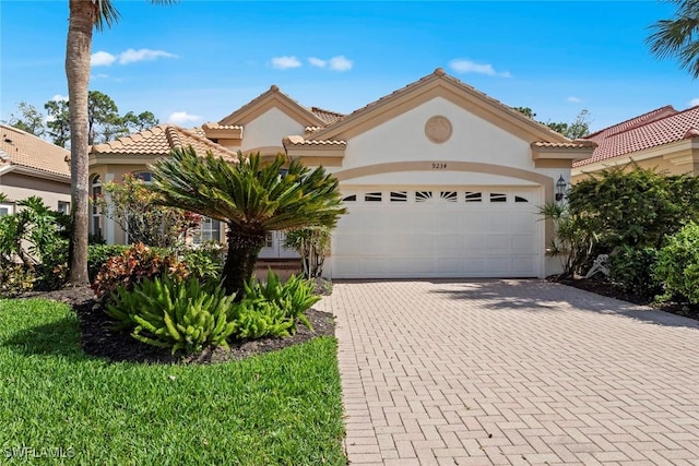 mediterranean / spanish-style house featuring a tiled roof, decorative driveway, an attached garage, and stucco siding