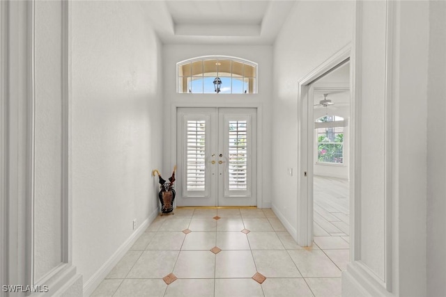 foyer featuring a wealth of natural light, a raised ceiling, baseboards, and light tile patterned floors