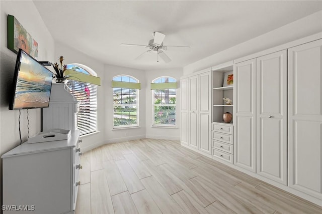 interior space featuring a ceiling fan, baseboards, multiple closets, and wood finish floors