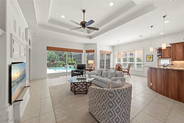 living room featuring ceiling fan, a tray ceiling, light tile patterned flooring, and baseboards