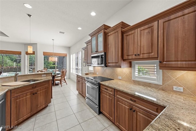 kitchen with brown cabinets, light stone countertops, stainless steel appliances, pendant lighting, and a sink