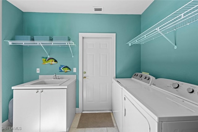 laundry area with cabinet space, light tile patterned floors, visible vents, washing machine and dryer, and a sink