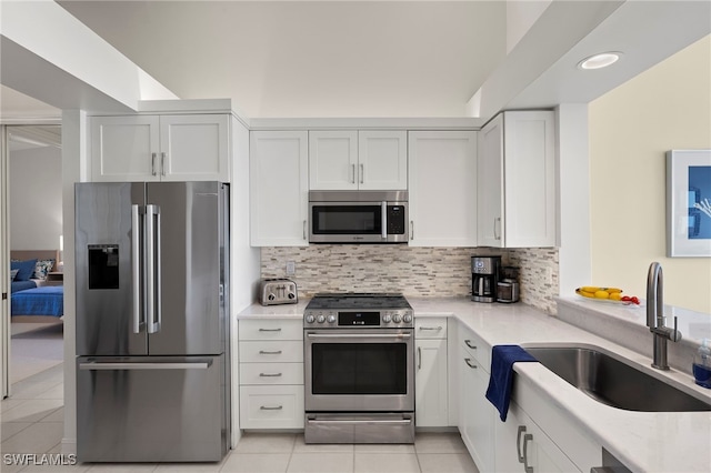 kitchen with light tile patterned flooring, a sink, white cabinetry, appliances with stainless steel finishes, and decorative backsplash