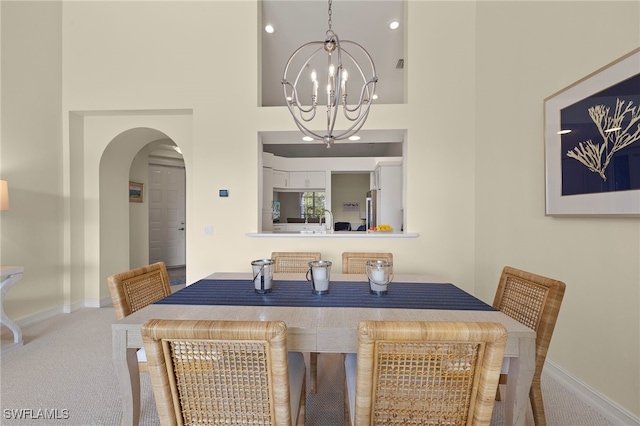 dining space featuring arched walkways, a notable chandelier, a high ceiling, carpet flooring, and baseboards