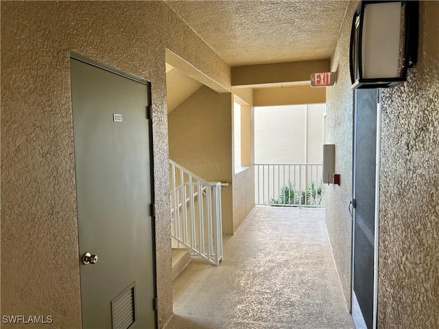 hallway with visible vents, a textured wall, stairs, concrete flooring, and a textured ceiling