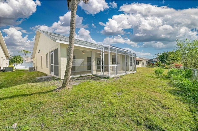 back of house with central air condition unit, glass enclosure, a lawn, and stucco siding