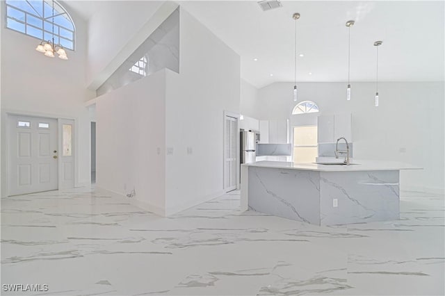 kitchen with marble finish floor, decorative light fixtures, freestanding refrigerator, white cabinets, and a sink