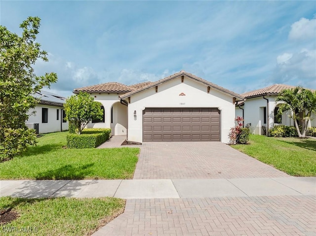 mediterranean / spanish-style house featuring an attached garage, a tile roof, decorative driveway, and a front yard