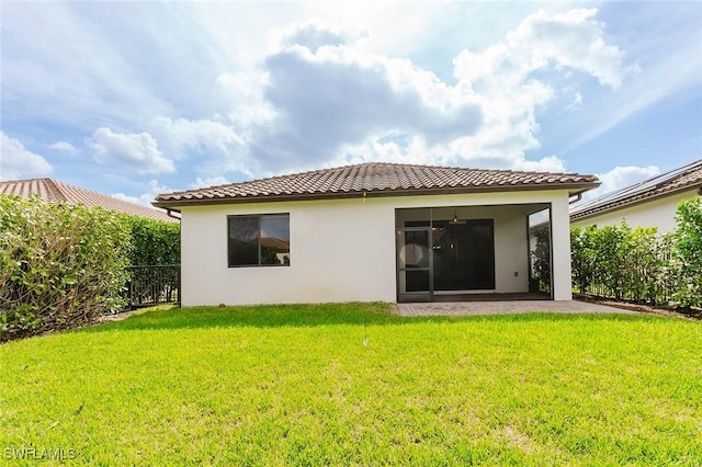 rear view of house featuring stucco siding, a tile roof, a lawn, and fence