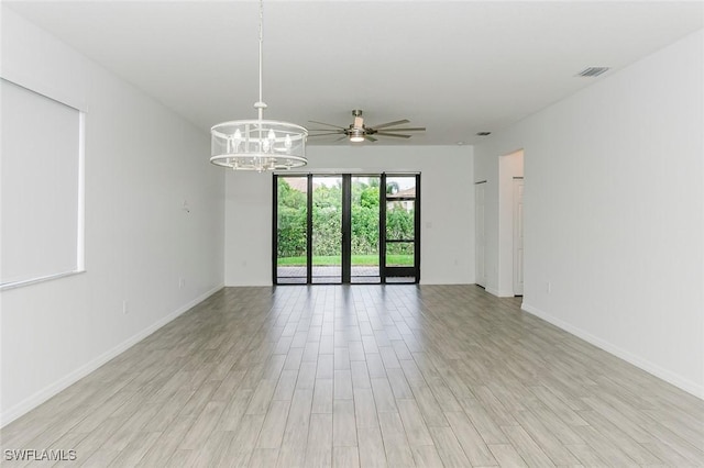 unfurnished room featuring ceiling fan with notable chandelier, light wood finished floors, visible vents, and baseboards