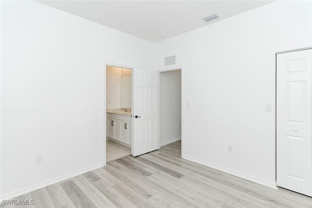 unfurnished bedroom with light wood-type flooring, ensuite bath, baseboards, and visible vents