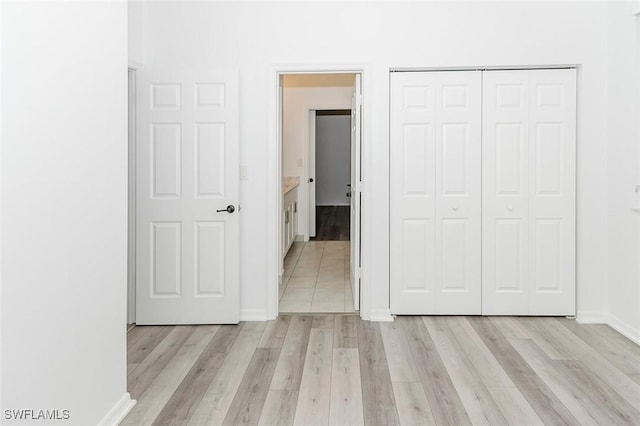 unfurnished bedroom featuring light wood-type flooring, a closet, and baseboards