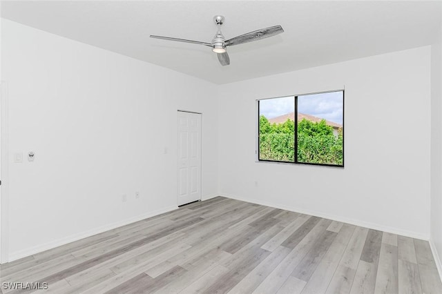 empty room featuring light wood finished floors, baseboards, and a ceiling fan