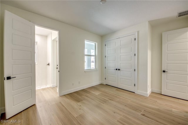 unfurnished bedroom featuring baseboards, a closet, visible vents, and light wood-style floors