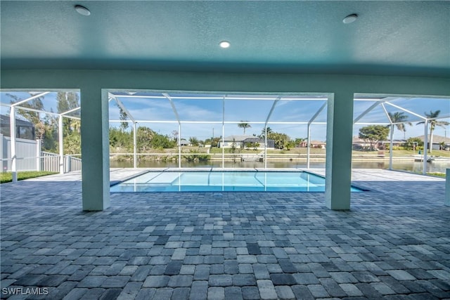 view of pool featuring a patio area, glass enclosure, a water view, and fence