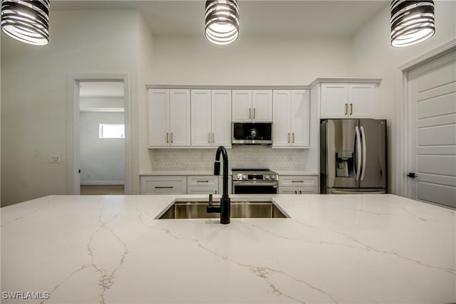 kitchen featuring white cabinets, appliances with stainless steel finishes, backsplash, light stone counters, and a sink