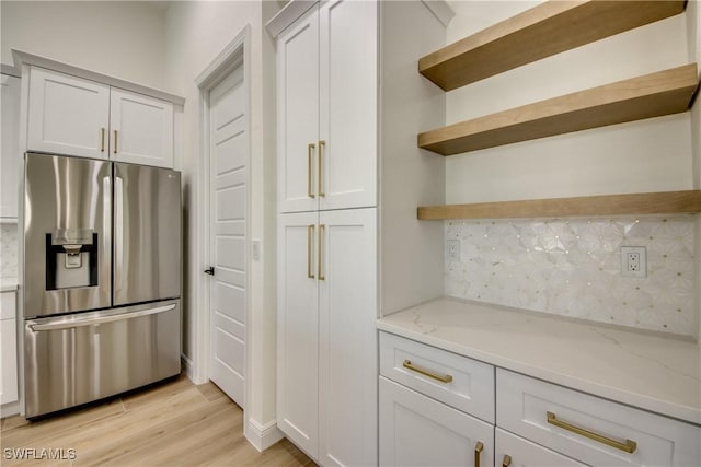 kitchen with light stone counters, stainless steel fridge, white cabinetry, and open shelves