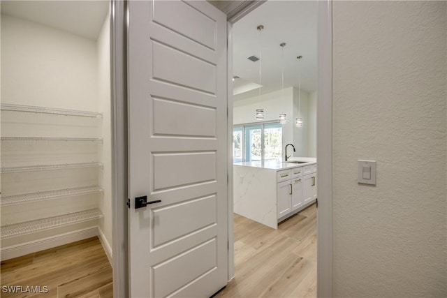 corridor featuring a textured wall, a sink, visible vents, baseboards, and light wood finished floors