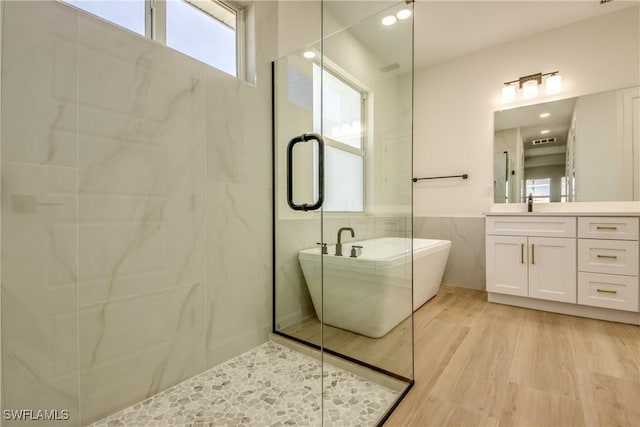 bathroom featuring a freestanding tub, wood finished floors, vanity, tile walls, and an enclosed shower