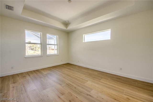 spare room with light wood-type flooring, a raised ceiling, and visible vents