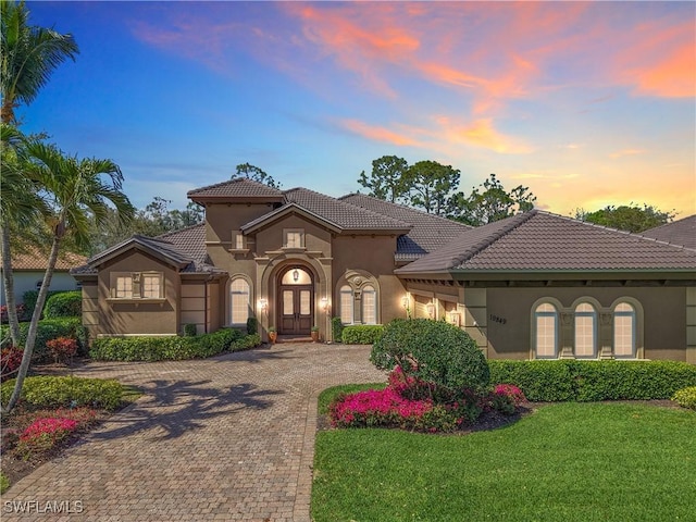 mediterranean / spanish home with a tiled roof, decorative driveway, a lawn, and stucco siding