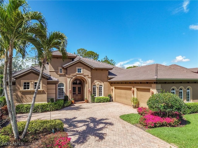 mediterranean / spanish house with a garage, a tiled roof, decorative driveway, and stucco siding