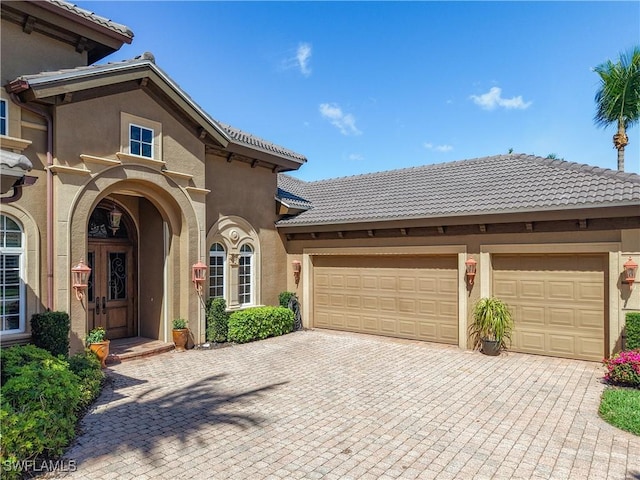 mediterranean / spanish home with a garage, decorative driveway, a tile roof, and stucco siding